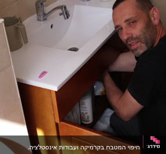 אדם מתקן ארון מתחת לכיור בחדר אמבטיה